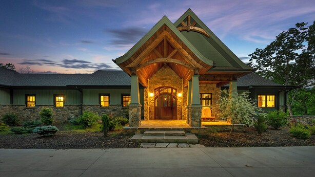A two-story house with a stone facade, a wooden porch, and a green roof.