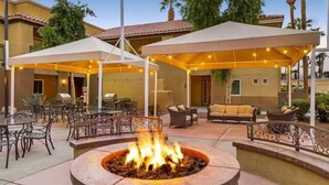 Ein Außenbereich mit einer Feuerstelle, überdachter Sitzgelegenheit und Tischen.