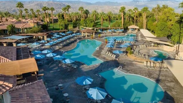 Ein Resort mit mehreren Schwimmbecken, Liegebereichen mit Sonnenschirmen und Blick auf Berge.