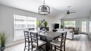 A spacious dining area with a large table and chairs, a ceiling fan, and a view of the outdoors through large windows.