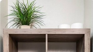 A wooden shelf unit with a potted plant, rolled towels, toiletries, and a vase with flowers.