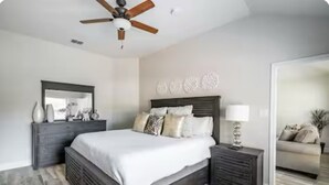 A bedroom with a bed, nightstands, a dresser, a ceiling fan, a mirror, and a wall with decorative plates.