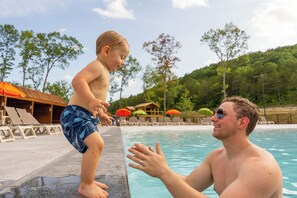 Un hombre y un niño junto a una piscina con tumbonas y sombrillas al fondo.
