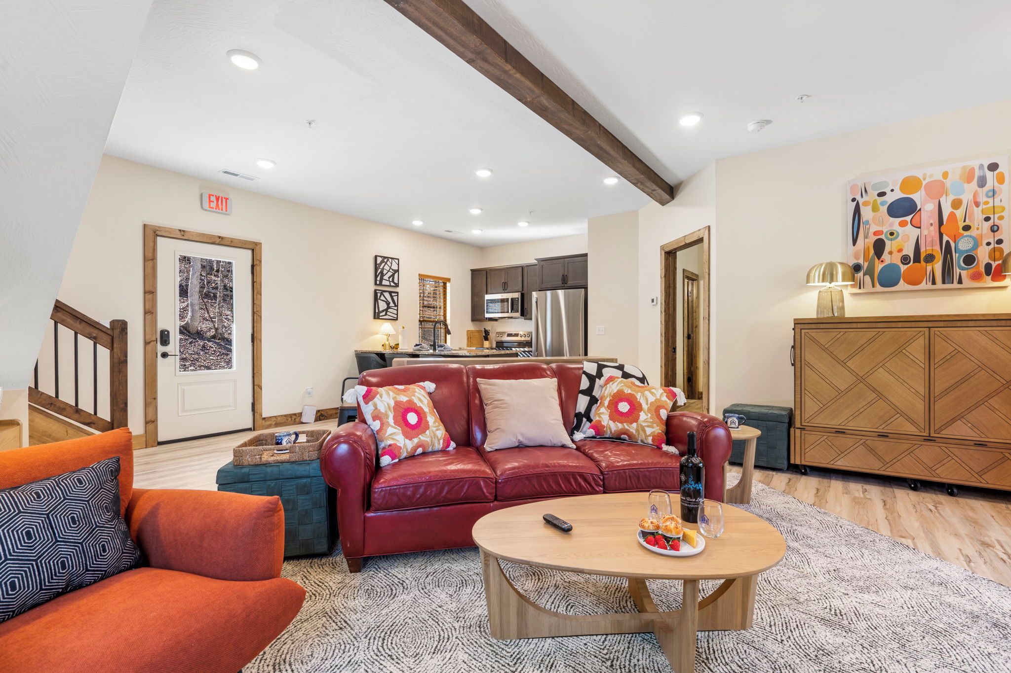 A modern living room with a red leather sofa, a wooden coffee table, and a kitchen in the background.