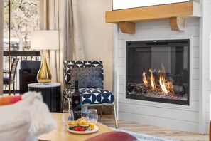 Una sala de estar acogedora con chimenea, un sillón estampado, una mesa con fresas y una botella de vino.