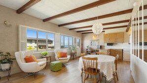 A spacious living area with a dining table, two armchairs, a sofa, and a kitchen area with wooden cabinets.