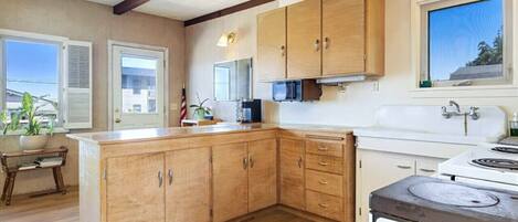 A kitchen with wooden cabinets, a stove, and a window with blinds.