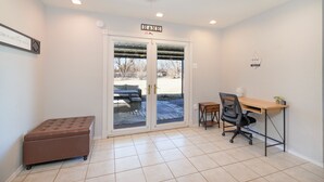 A room with a sliding glass door leading to a patio, a wooden desk with a chair, and a small ottoman. - Cozy Home 4 Minutes from Fort Sill (Lawton)