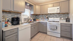 A modern kitchen with grey cabinets, a white microwave, a coffee maker, and a tiled backsplash. - Cozy Home 4 Minutes from Fort Sill (Lawton)