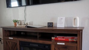 A wooden entertainment center with a flat-screen TV mounted above, a tablet, a sign with 'HUMAN-KIND' written on it, and a Scrabble box. - Cozy Home 4 Minutes from Fort Sill (Lawton)