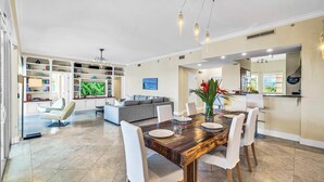 A spacious living area with a dining table, chairs, a sofa, and a kitchen in the background. - Ocean View Penthouse | Retreat amenities: tennis court, heated Pool | Vista Key Two (Islamorada)
