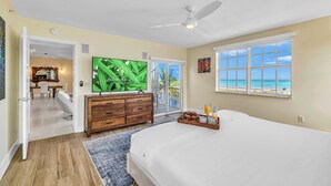 A bedroom with a large bed, a ceiling fan, a TV, and a view of the beach. - Ocean View Penthouse | Retreat amenities: tennis court, heated Pool | Vista Key Two (Islamorada)
