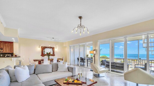 A spacious living room with a large sofa, a coffee table with fruit and cheese, a dining area with chairs, and a view of the ocean through large sliding doors. - Ocean View Penthouse | Retreat amenities: tennis court, heated Pool | Vista Key Two (Islamorada)