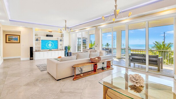 Ein geräumiges Wohnzimmer mit großem Fernseher, einer Couch, einem Glastisch und einem Balkon mit Meerblick.