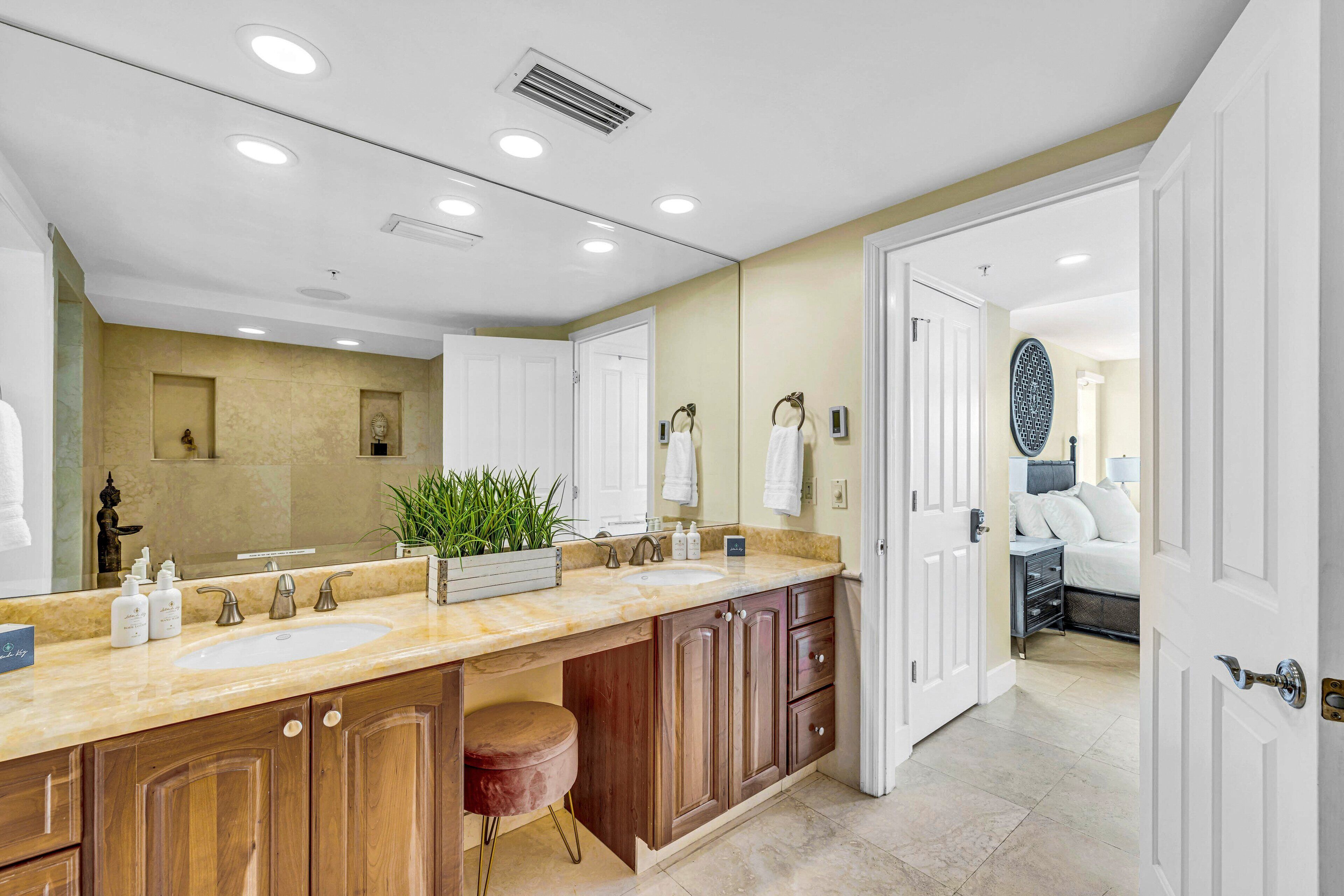 A modern bathroom with a large mirror, two sinks, wooden cabinets, and a vanity with a stool.