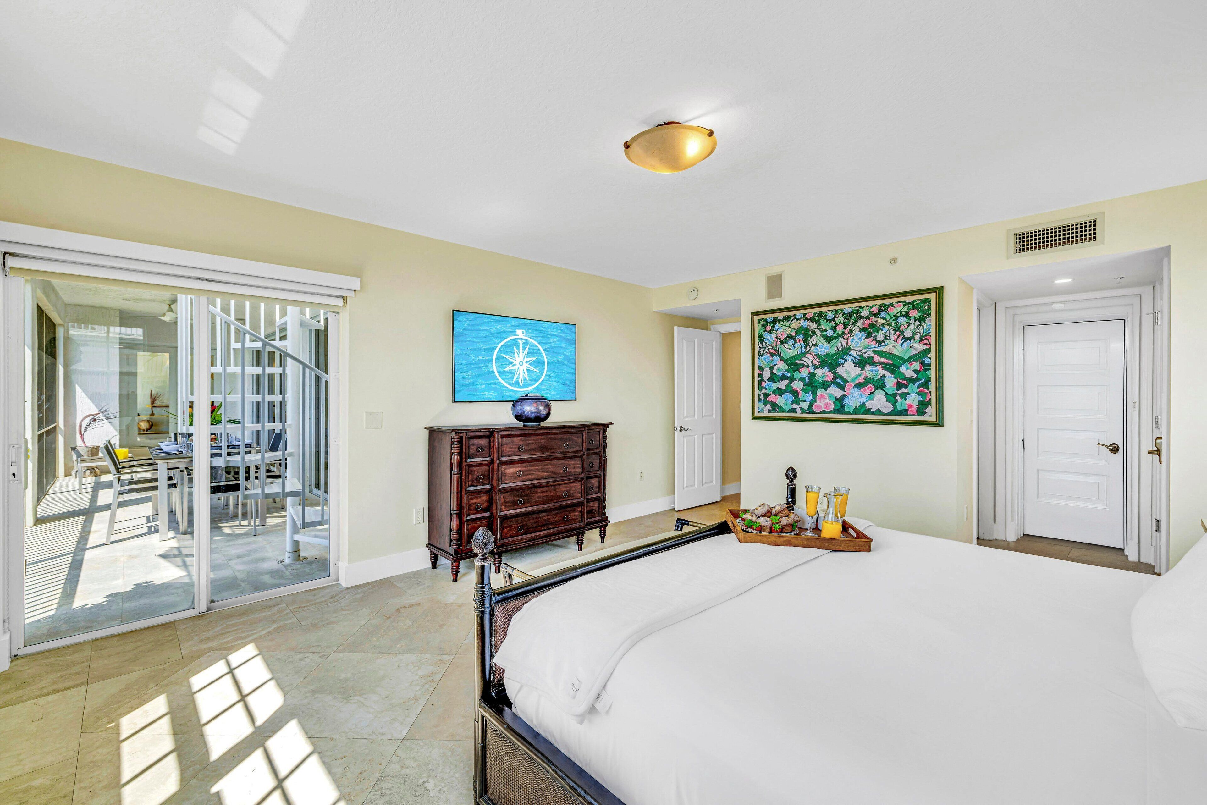 A bedroom with a large bed, a dresser, a painting, and a sliding glass door leading to a balcony.
