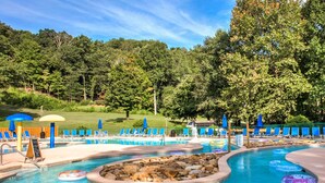 Une piscine entourée d’arbres et d’une pelouse, avec des chaises longues et des parasols.