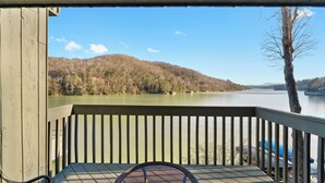 Une terrasse en bois offrant une vue sur un lac et des collines boisées.