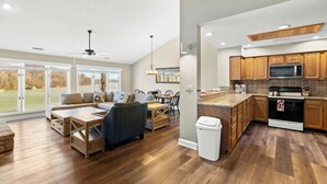 Un salon spacieux doté d’une grande fenêtre, d’un coin repas et d’une cuisine avec des meubles en bois et des appareils modernes.