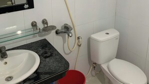 Een badkamer met een wit toilet, een wastafel met een zwart aanrechtblad, een spiegel met bladdecoraties, en een handdouche.