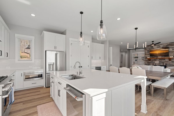 Una cocina moderna con armarios blancos, electrodomésticos de acero inoxidable e iluminación colgante.