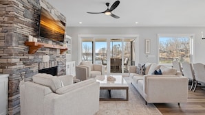 A modern living room with a stone fireplace, comfortable seating, and large windows offering a view of the outdoors.