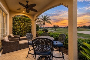 A covered outdoor seating area with wicker furniture and a view of a golf course at sunset. - Theater, Games Area | Golf Course Views | Private Pool | Golf Course Views (Kissimmee)