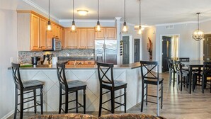 A modern kitchen with wooden cabinets, a central island with bar stools, stainless steel appliances, and pendant lighting. - Lands End Condo with Amazing Main Channel Views, 2 Pools, Playground & Boat Slip (Osage Beach)