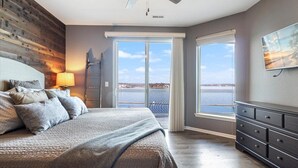A bedroom with a bed, a dresser, a ceiling fan, a window with a view, and a painting on the wall. - Lands End Condo with Amazing Main Channel Views, 2 Pools, Playground & Boat Slip (Osage Beach)