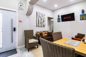 A furnished room with a sofa, chairs, a table, a television, and a wall-mounted artwork.