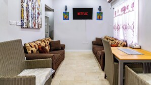 Kalustettu olohuone, jossa on kaksi sohvaa, puinen pöytä ja seinälle asennettu televisio, jonka näytöllä näkyy teksti ’NETFLIX’.