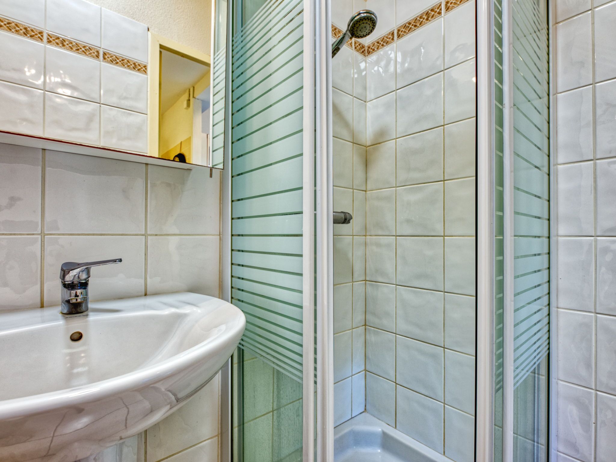 Une salle de bain avec un lavabo blanc, une cabine de douche en verre et des murs carrelés.