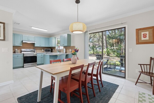 A modern kitchen with light blue cabinets, a central island, and a dining area with wooden chairs. - Quiet Charm: Central Island Convenience (Fernandina Beach)