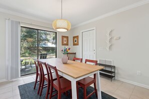 A dining area with a wooden table and red chairs, a woven pendant light, and a view through a sliding glass door to an outdoor patio. - Quiet Charm: Central Island Convenience (Fernandina Beach)