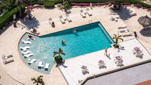 Une piscine rectangulaire dotée d’un espace aménagé autour, bordée de chaises longues et d’une plage de sable.