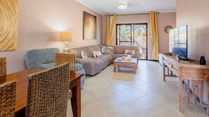 Un salon avec un canapé, une table à manger et des chaises, un téléviseur et une fenêtre avec des rideaux.