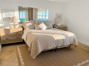 A bedroom with a bed, bedside tables, lamps, and a view of the sea. - Direct Ocean & Pool Views, Fully Updated 1-BD Condo on FMB. 105A (Fort Myers Beach)