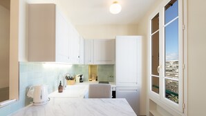 A modern kitchen with white cabinets, a marble countertop, and a window with a view of buildings. - Renovated apartment near the beach (Antibes)