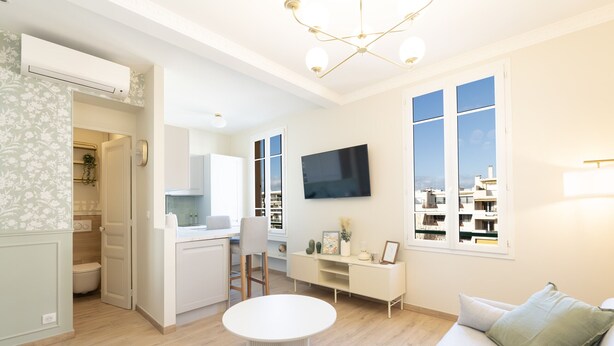 A modern living room with a white sofa, a round table, and a TV mounted on the wall. - Renovated apartment near the beach (Antibes)