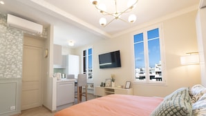 A hotel room with a large bed, a desk, a chair, a TV, and a view of the city through the window. - Renovated apartment near the beach (Antibes)