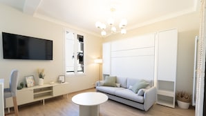 A modern living room with a flat-screen TV, a sofa, a coffee table, and a large window. - Renovated apartment near the beach (Antibes)