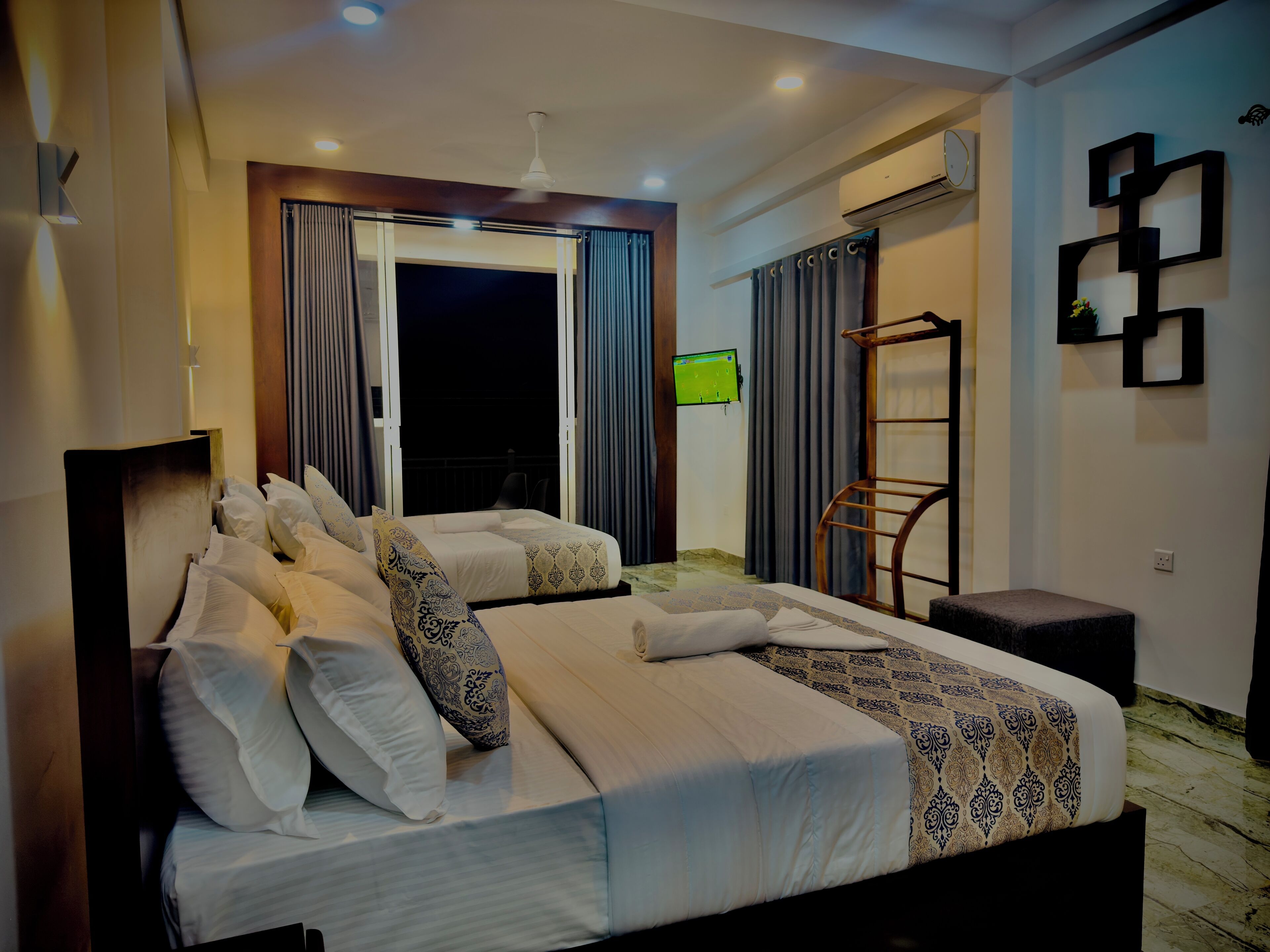 Habitación de hotel con dos camas, televisión, aire acondicionado y balcón con cortinas.