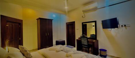 Habitación de hotel con cama, escritorio, silla, armario, televisor y baño.