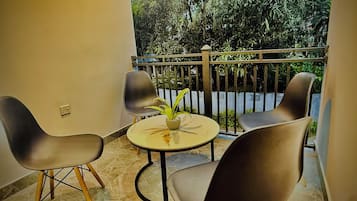 A balcony with two chairs and a small table, a potted plant, and a view of greenery.