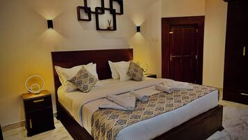 Una cama bien hecha con un edredón estampado, dos mesitas de noche con lámparas, una lámpara de pared y una puerta de madera.