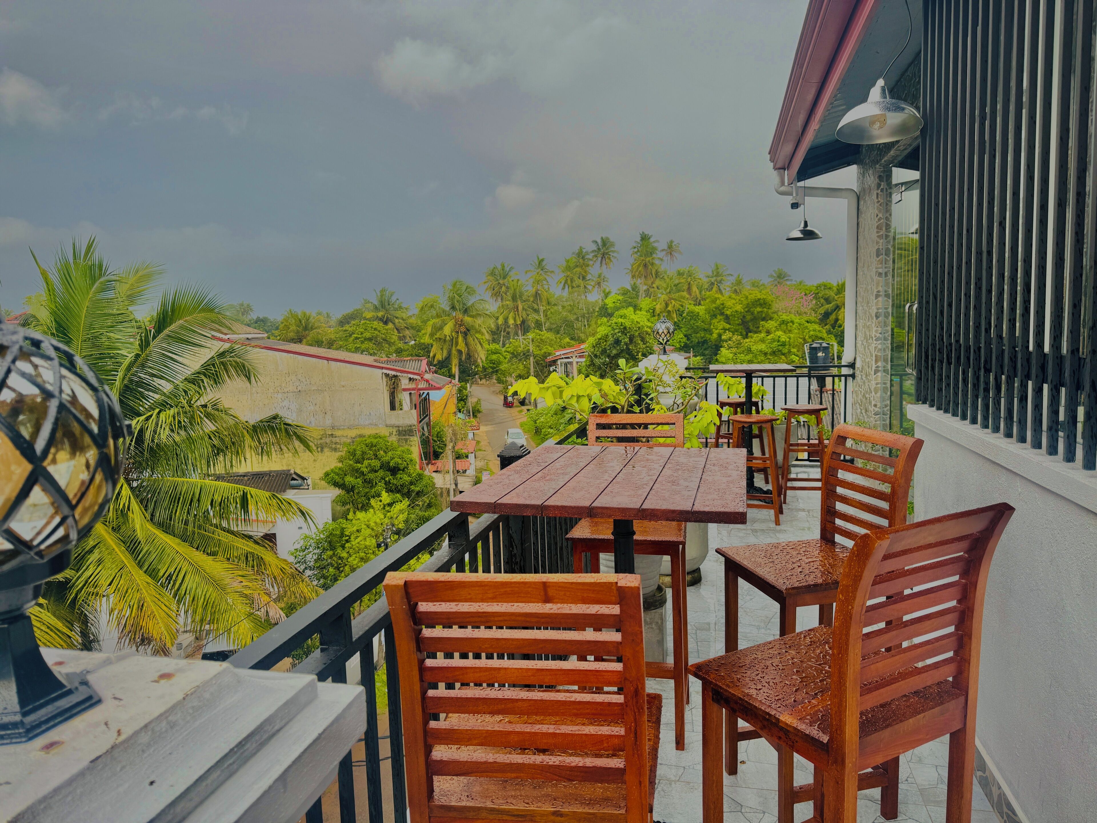 A balcony with wooden furniture, a view of a street, and palm trees.