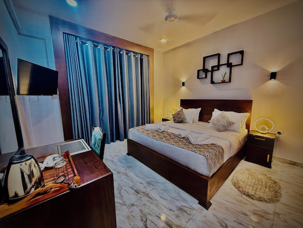 Una habitación de hotel moderna con una cama grande, una mesita de noche con lámpara, un televisor y una cortina.