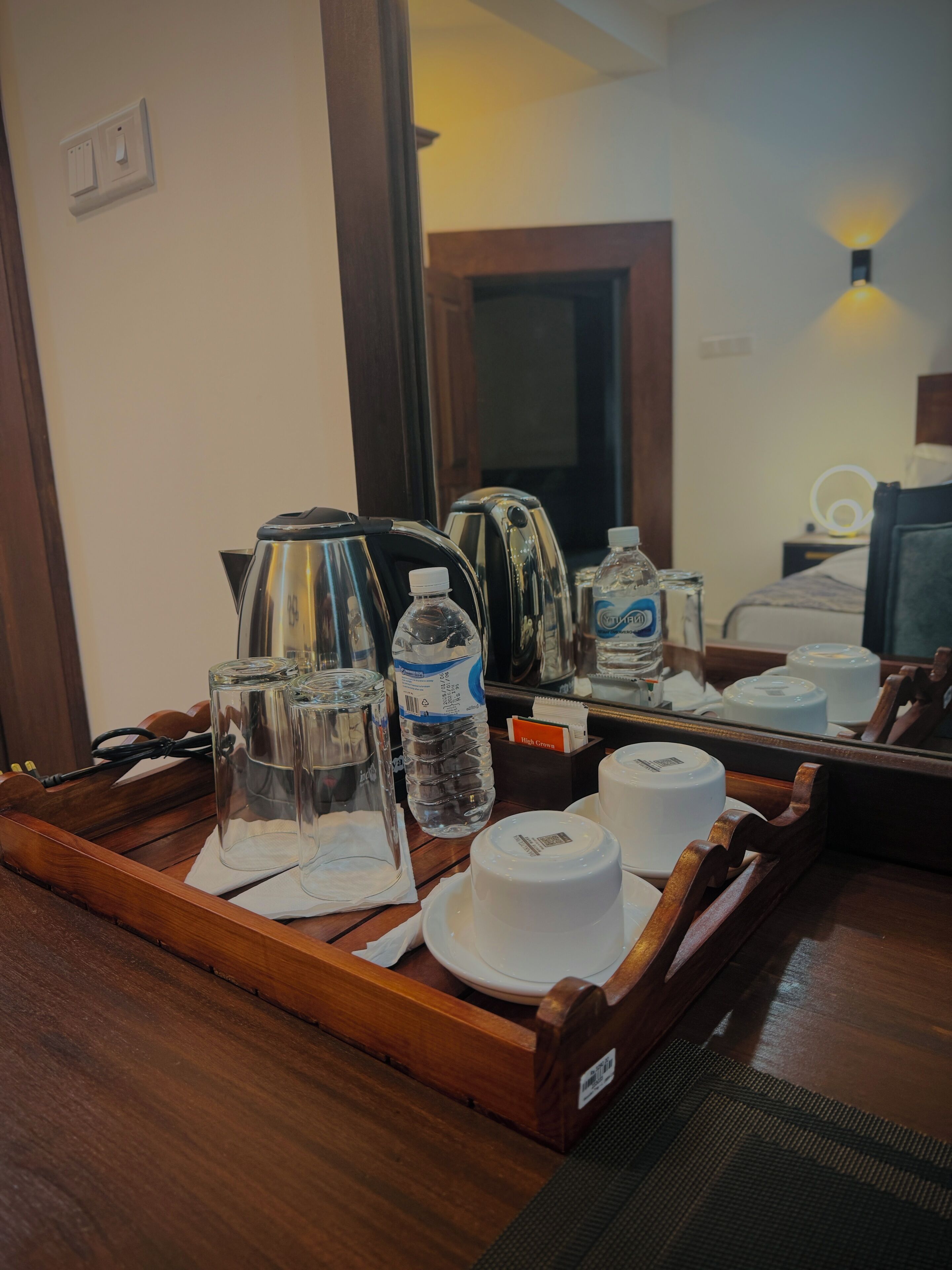Una bandeja de madera con una tetera, botellas de agua y tazas blancas sobre una mesa.