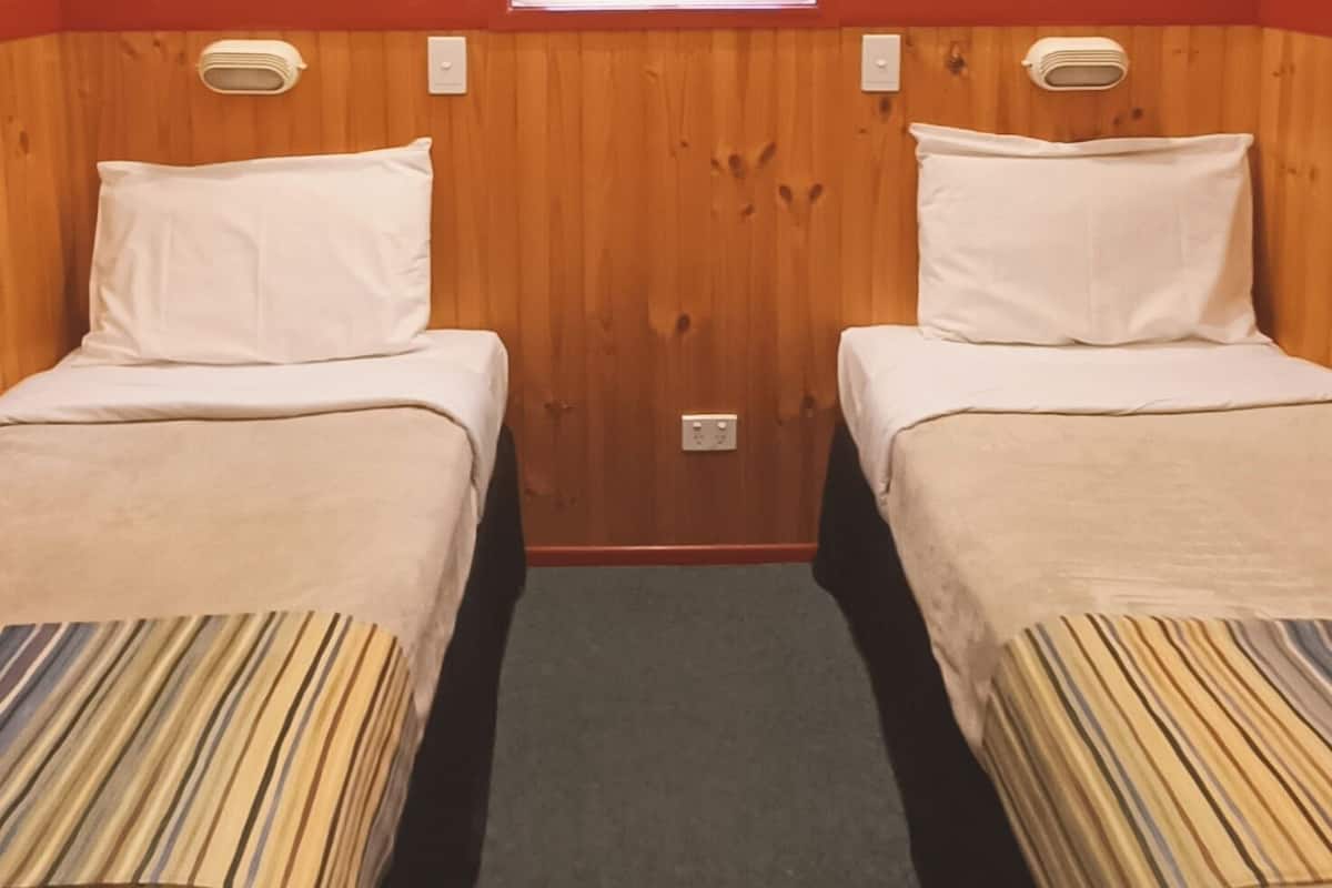 A room with two beds, a ceiling fan, a window with blinds, and a thermostat on the wall.