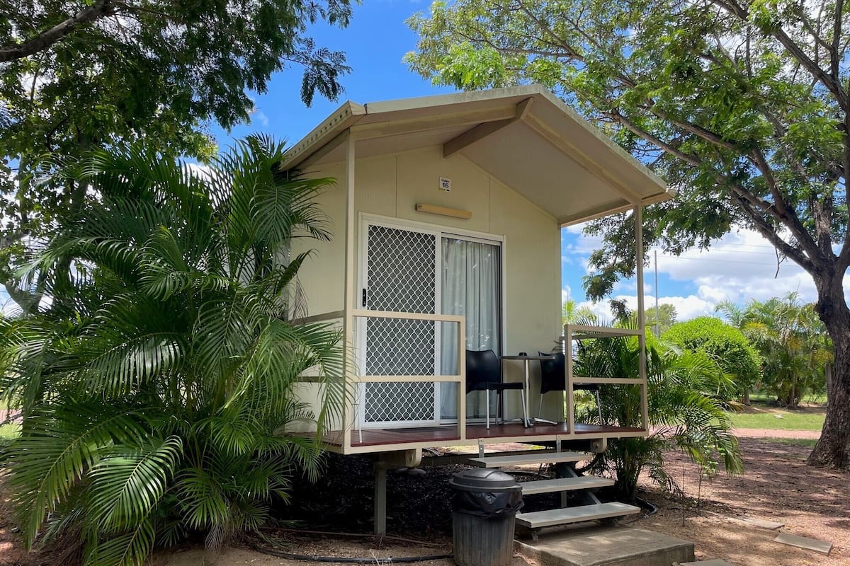 A small, single-story cabin with a covered porch, a sliding glass door, and a trash bin.